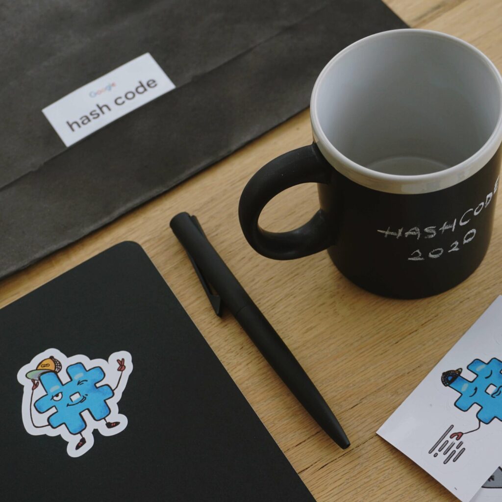 hash code goodies: one cool dark pen, one cool dark notebook with a custom sticker, one cool dark mug